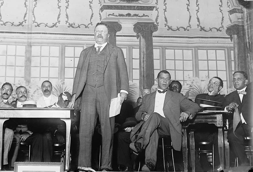 Via Wikimedia Commons President Roosevelt addresses the National Negro Business League in 1910 as Booker T. Washington is seated behind him at right.